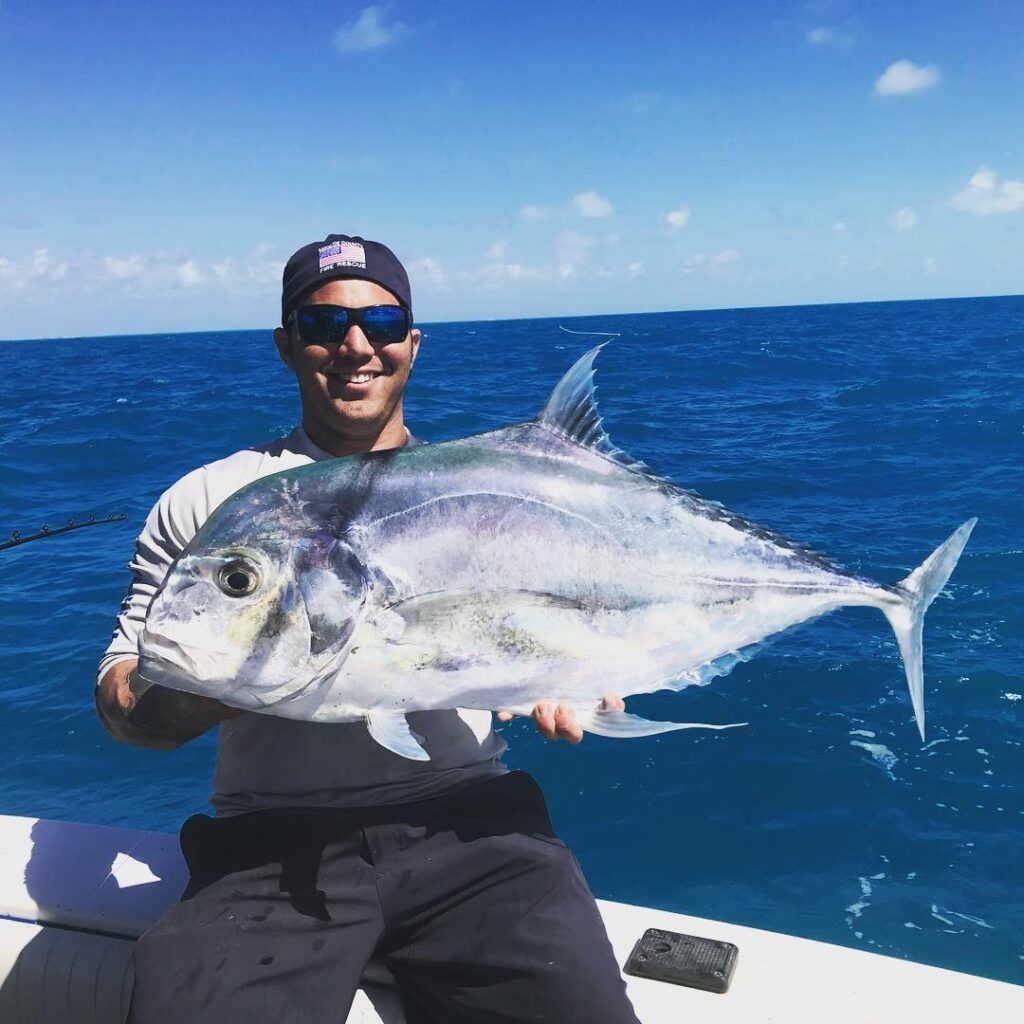 A beaming fisherman wearing a cap and sunglasses on a sunny day, proudly holding up a large, impressive catch on a boat, representing the successful outings led by Key West fishing guides.